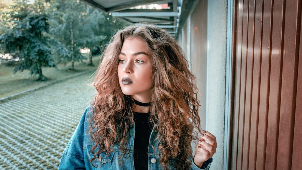A young woman with curly hair posing in front of a building.