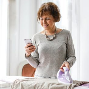 a beautiful woman looking at her phone while ironing