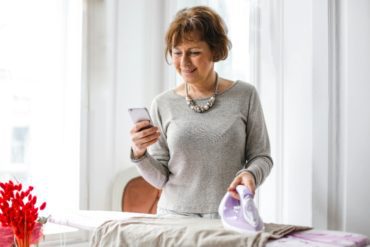a beautiful woman looking at her phone while ironing