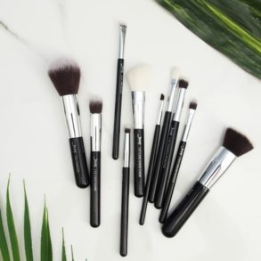 Makeup brushes on a white surface with green leaves