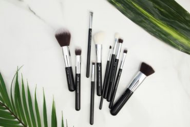 Makeup brushes on a white surface with green leaves