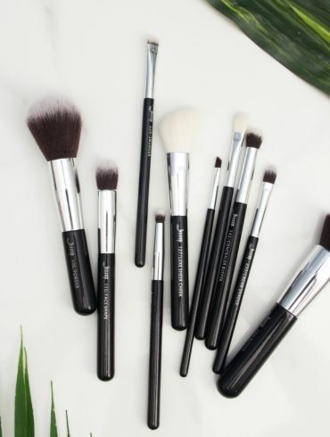 Makeup brushes on a white surface with green leaves